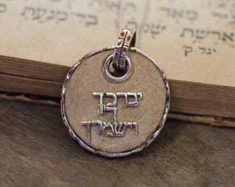 May include: A silver pendant necklace with a round, cream-colored charm. The charm has Hebrew writing that reads "Shema Yisrael" which translates to "Hear O Israel".