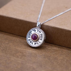 May include: Silver and gold tone necklace with a round pendant featuring Hebrew text and a red gemstone.