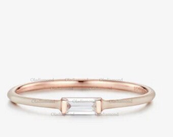 May include: A delicate rose gold band ring with a single, clear, rectangular-shaped diamond set in the center.