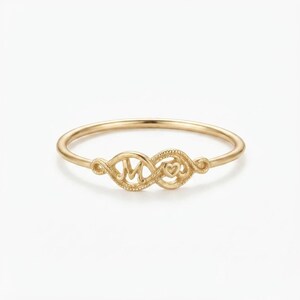 May include: A gold ring featuring a thin, polished band. The centrepiece consists of an infinity-shaped design with a textured surface, displaying the letter M on the left side and a small heart symbol on the right side of the loop.