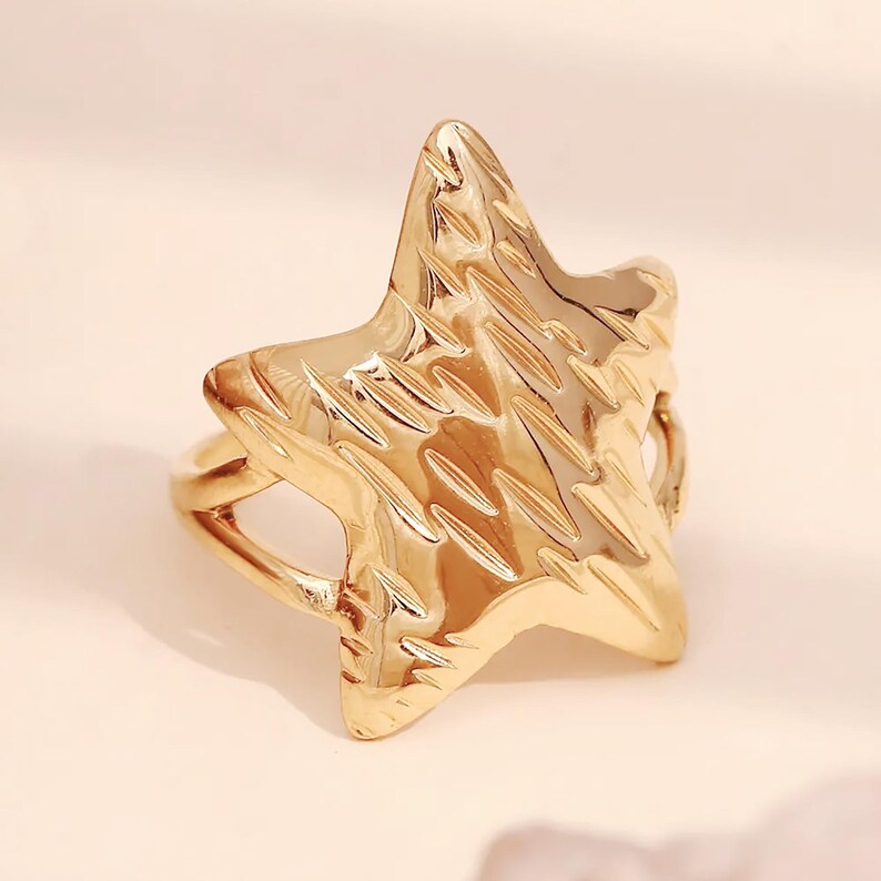 May include: A gold-toned ring with a textured star-shaped design. The ring is open on one side and has a smooth band.