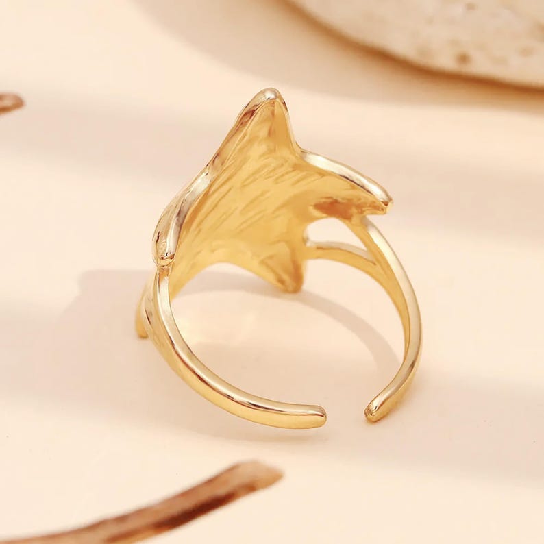 May include: Gold-toned adjustable ring with a star-shaped design. The ring is open in the back and has a smooth, polished finish.