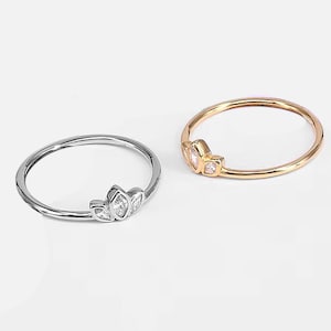 May include: Two simple rings with a small cluster of clear stones in the shape of leaves. The ring on the left is silver and the ring on the right is gold.