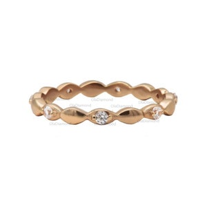 May include: A gold-colored ring with a repeating pattern of oval shapes, each holding a small, clear gemstone. The ring has a delicate, feminine design, suitable for everyday wear or special occasions. The ring is set against a white background.