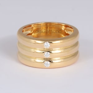 May include: A gold band ring with three round diamonds set in the center of the band. The band is thick and has a smooth, polished finish.
