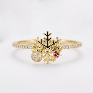 Peut inclure: Une bague en or ornée d'un motif central en forme de flocon de neige, agrémentée d'une petite breloque sphérique pendante recouverte de pierres claires et d'un groupe de trois pierres rouges, avec un anneau serti de pierres claires.