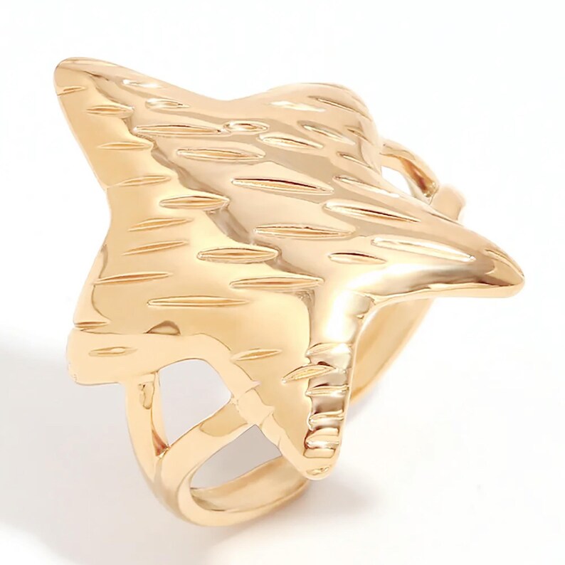 May include: A gold-toned ring with a textured star-shaped design. The ring is open on one side and has a smooth band.