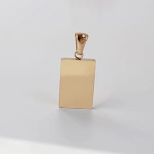 Könnte beinhalten: Ein goldfarbener rechteckiger Anhänger mit einer kleinen Schlaufe oben für eine Kette. Der Anhänger hat eine glatte, reflektierende Oberfläche und ein schlichtes, minimalistisches Design. Der Anhänger ist wahrscheinlich aus Metall und für den Alltag geeignet.