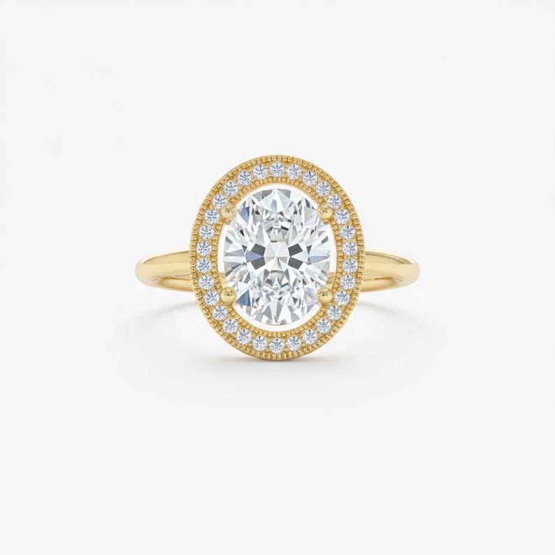 K&ouml;nnte beinhalten: Ein goldener Verlobungsring mit einem oval geschliffenen Diamanten. Der Diamant ist von einem Halo aus kleineren Diamanten umgeben. Der Ring hat ein detailliertes Band.