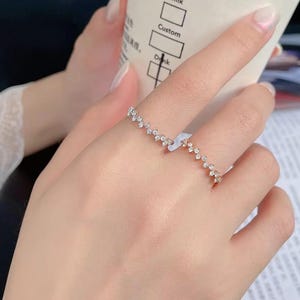 Op de afbeelding: Een zilverkleurige open ring met een reeks kleine, sprankelende stenen gerangschikt in een golfpatroon. Het minimalistische ontwerp van de ring is geschikt voor dagelijks gebruik of speciale gelegenheden. De ring is elegant en zou een ideaal cadeau zijn.