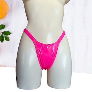 Könnte beinhalten: Hellrosa String-Unterwäsche mit glänzendem, Wet-Look-Finish. Das Kleidungsstück wird auf einer Schaufensterpuppe präsentiert, die das schlanke Design und die leuchtende Farbe hervorhebt. Die Kanten sind sauber genäht, und die Gesamtästhetik ist modern und minimalistisch.