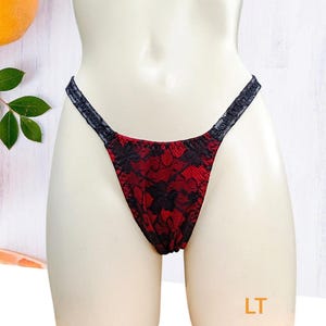 Puede incluir: Ropa interior de encaje roja con ribete negro. La ropa interior tiene un patrón floral y se muestra en un maniquí blanco.