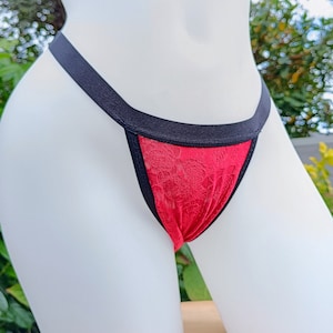 Puede incluir: Ropa interior de encaje roja con ribete negro. La ropa interior se muestra en un maniquí blanco.