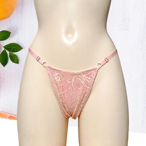 Puede incluir: Ropa interior de encaje rosa con un delicado patrón floral. La ropa interior tiene tirantes ajustables y un corte de talle bajo.