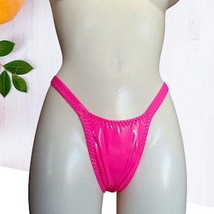 May include: Bright pink thong-style underwear with a shiny, wet-look finish. The garment is displayed on a white mannequin, showcasing its sleek design and minimal coverage. The edges are neatly stitched.