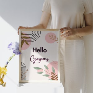Puede incluir: Una impresión enmarcada con fondo blanco y formas abstractas rosas, marrones y verdes. El texto "Hello Gorgeous" está escrito en letras negras y rosas.