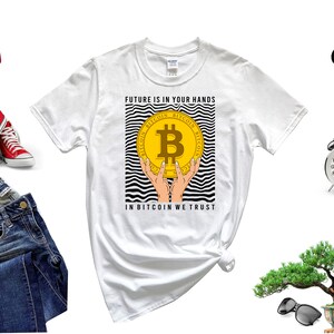 May include: White t-shirt with a black and white striped design featuring a gold Bitcoin coin with the text "FUTURE IS IN YOUR HANDS" and "IN BITCOIN WE TRUST".