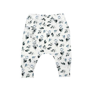 Peut inclure: Pantalon de bébé blanc avec un motif floral. Le pantalon présente un motif répété de fleurs bleues et de feuilles vert foncé. Le tissu semble doux et confortable, avec une coupe décontractée et une taille élastique.