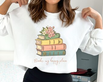 Può includere: Felpa bianca con una pila di libri sormontata da fiori. Il testo "Books: my happy place" è stampato sotto i libri.