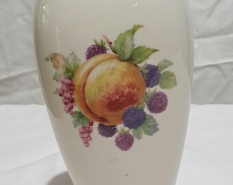 May include: Cream-colored ceramic vase with a gold rim and base. The vase features a painted design of a peach, grapes, and blackberries. The fruit is surrounded by green leaves. The vase has a smooth, glossy finish.