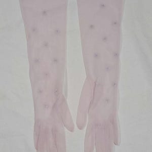 May include: A pair of pale pink sheer opera-length gloves made from a lightweight, translucent fabric. The gloves feature a scattered pattern of small, delicate, tonal embroidered floral accents across the surface of the hand and forearm.