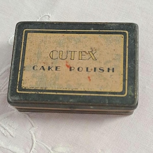 May include: A vintage black and gold tin box with the text "Cutex Cake Polish" on the front.