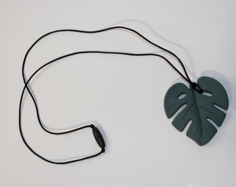 May include: A dark green silicone necklace with a monstera leaf pendant. The necklace is made of a soft, flexible material and is perfect for teething babies.
