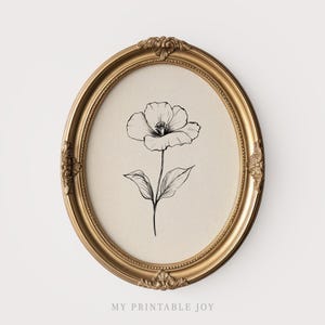 May include: A gold-coloured, oval frame contains a black and white botanical drawing of a flower. The flower has a long stem and leaves, set against a beige backdrop. The text "MY PRINTABLE JOY" is visible at the bottom of the frame.