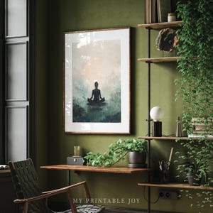 May include: A framed print of a silhouette of a person meditating in a peaceful, misty forest setting. The print is in a light wood frame and is hanging on a green wall. The image is a calming and serene depiction of mindfulness and meditation.