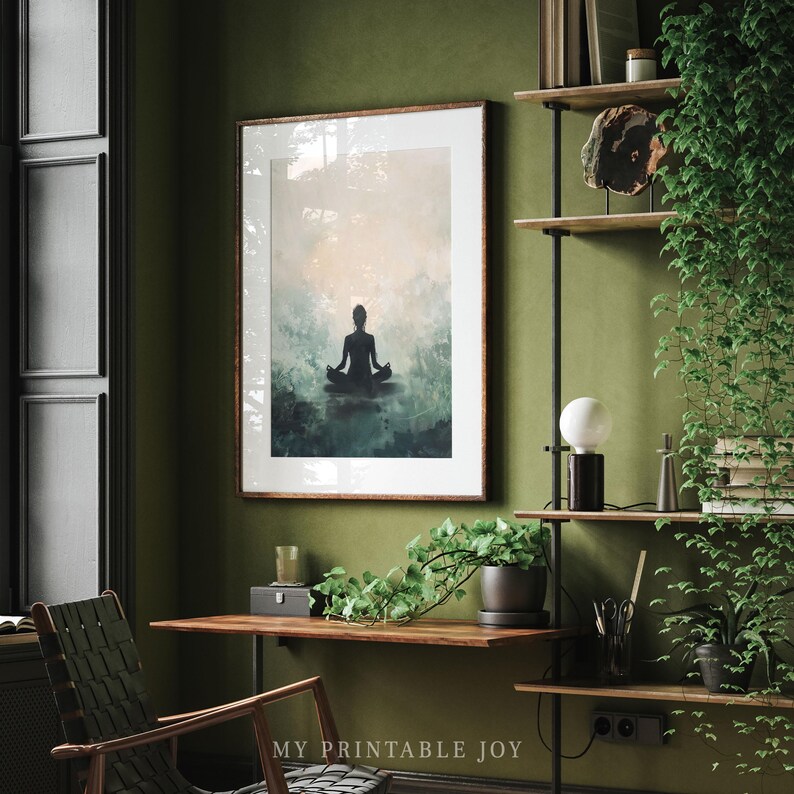 May include: A framed print of a silhouette of a person meditating in a peaceful, misty forest setting. The print is in a light wood frame and is hanging on a green wall. The image is a calming and serene depiction of mindfulness and meditation.