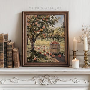Könnte beinhalten: Gerahmtes Gemälde eines Apfelhains mit einem Holzfass voller Äpfel. Das Bild hat einen braunen Holzrahmen und den Text "MY PRINTABLE JOY". Es steht auf einem weißen Kaminsims mit Büchern und Kerzen.