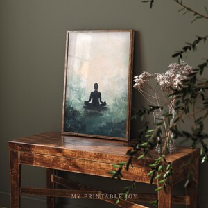 May include: A framed print of a silhouette of a person sitting in a yoga pose against a background of blue and green watercolor washes.