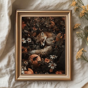 May include: A framed print featuring a sleeping fox nestled among pumpkins, flowers, and foliage in shades of orange, brown, and white. The artwork is set in a gold-colored frame, evoking a cozy autumn theme.