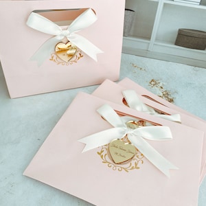 May include: Pink gift bags with white satin ribbon bows and gold heart-shaped tags. The tags have the text "Yuletide Wishes From" and "Mr. & Mrs. Santa".