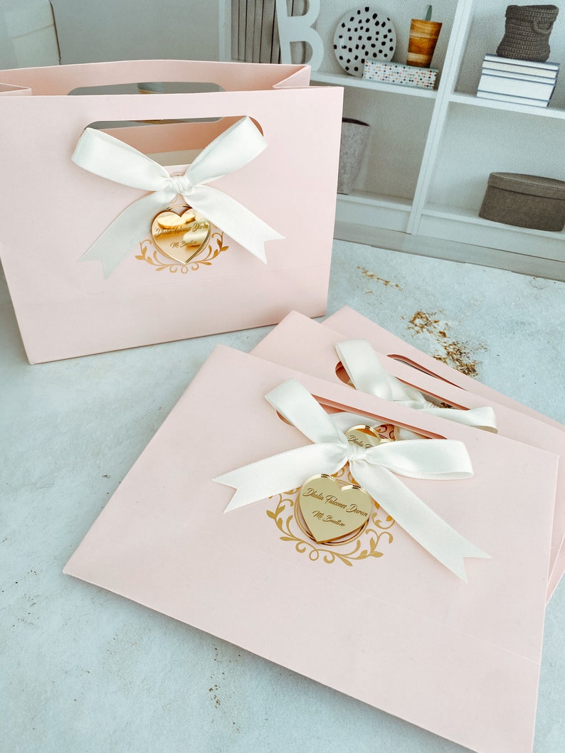 May include: Pink gift bags with white satin ribbon bows and gold heart-shaped tags. The tags have the text "Yuletide Wishes From" and "Mr. & Mrs. Santa".