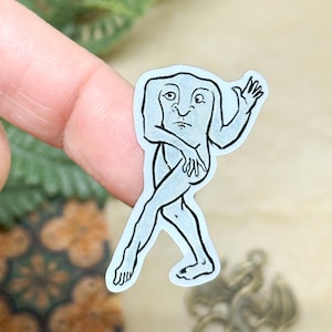 May include: A light blue sticker featuring a stylized illustration of a humanoid figure with a square head, arms, and legs. The figure is depicted in a walking pose, with one arm raised and the other crossed over its body. The sticker has a white border.