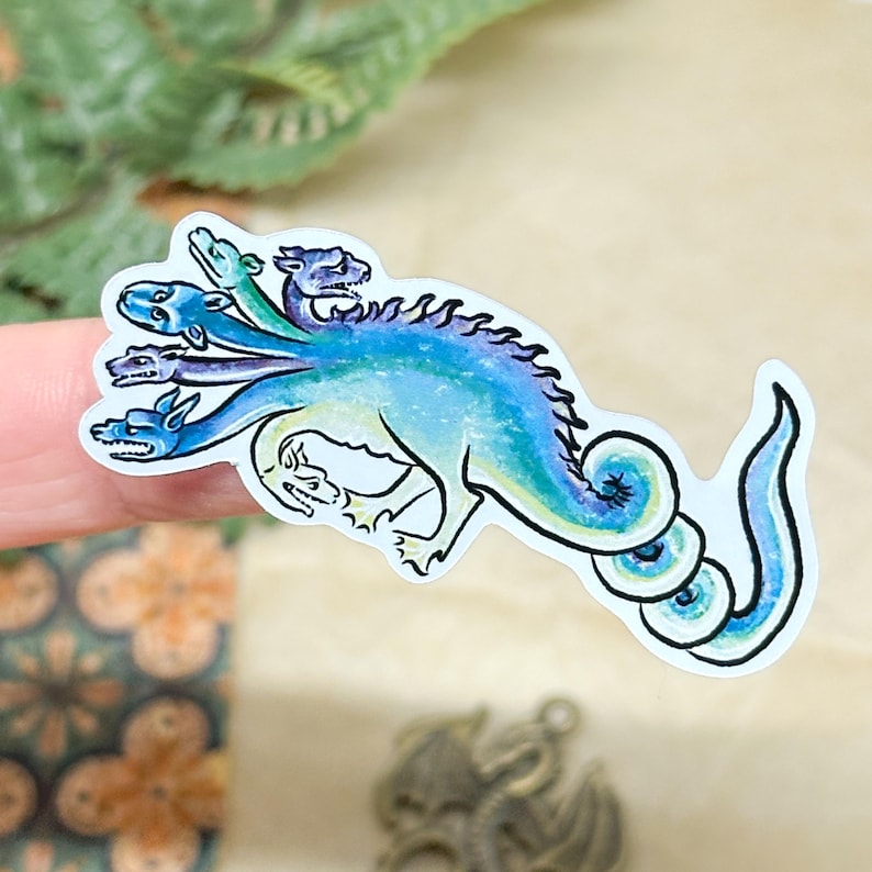 May include: A sticker featuring a multi-headed dragon in shades of blue and green. The dragon has a long, curved tail and a detailed, stylized design. The sticker is on a white background.