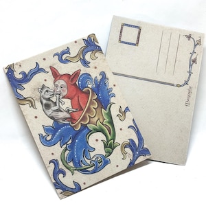 Puede incluir: Dos postales con ilustraciones de estilo medieval. Una muestra una figura de rojo sosteniendo un gato, rodeada de diseños florales azules y verdes. La otra tiene un reverso en blanco con líneas y un pequeño borde floral. El texto "Marginalia" es visible.