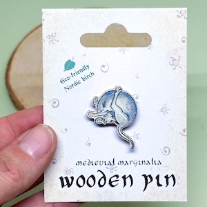 May include: A wooden pin depicting a blue and white cat curled up in a ball. The pin is made from eco-friendly Nordic birch and is labelled "medieval marginalia wooden pin".
