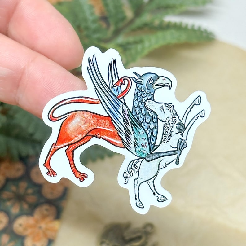 May include: A sticker featuring a mythical creature design. The sticker depicts a griffin with a red body, blue and white wings, and a horse-like creature. The artwork has a vintage, hand-drawn style with a white border.
