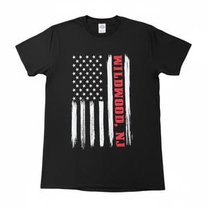 May include: Black t-shirt featuring a distressed American flag design. The flag has white stripes and stars, with the text "Wildwood, NJ" in red on the right side. A classic crew neck tee.