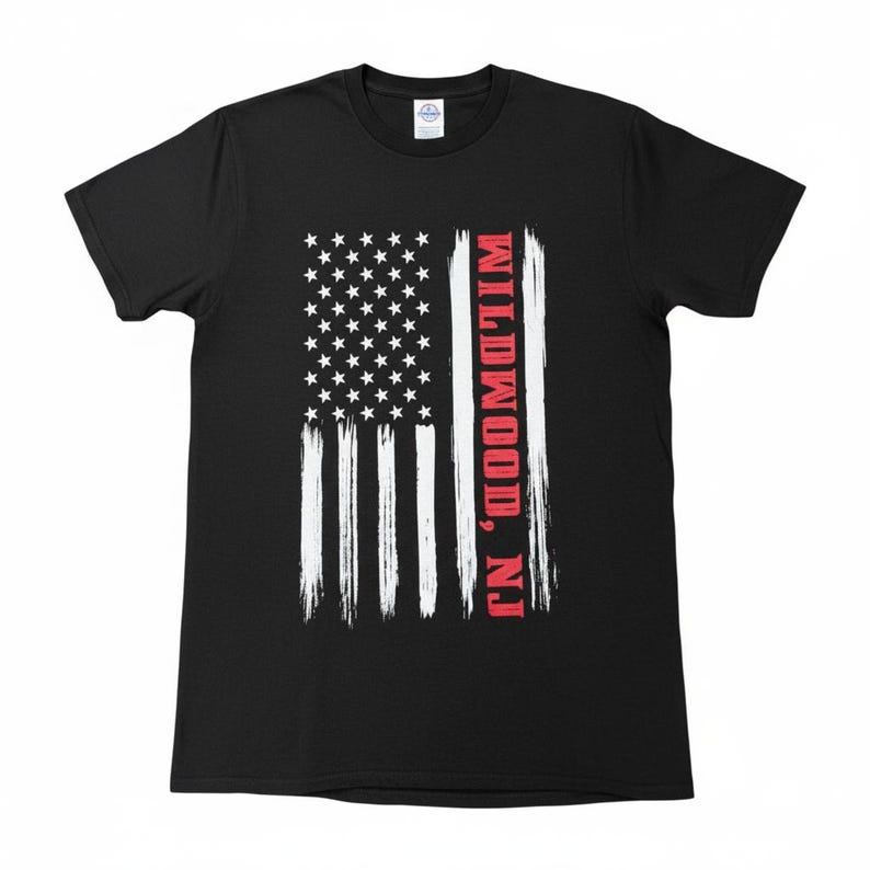 May include: Black t-shirt featuring a distressed American flag design. The flag has white stripes and stars, with the text "Wildwood, NJ" in red on the right side. A classic crew neck tee.