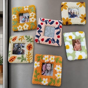 May include: Five square punch needle photo frames with textured yarn designs. One frame features yellow flowers, one has sunflowers, one displays autumn leaves, one shows a floral pattern on pink, and one has white daisies on green.