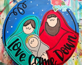 May include: A round, hand-painted wooden sign with a religious theme. The sign features a blue background with white stars and the words "Love Came Down." It depicts a family in red, teal, and gray robes. A flower sticker is in the upper right corner.
