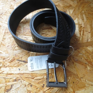 Peut inclure: Une ceinture en cuir noir avec une boucle argentée. La ceinture a un motif texturé et est enroulée.