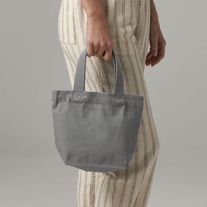 K&ouml;nnte beinhalten: Eine kleine, einfarbig graue Canvas-Tragetasche mit zwei stabilen Stoffgriffen, die mit verst&auml;rkten N&auml;hten befestigt sind. Die Tasche hat ein schlichtes Design mit offener Oberseite und einem strukturierten Boden f&uuml;r eine kompakte Aufbewahrung.