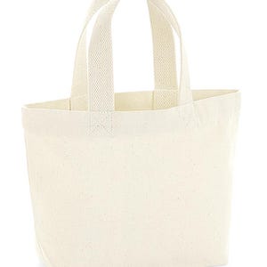 K&ouml;nnte beinhalten: Eine schlichte, cremewei&szlig;e Canvas-Einkaufstasche mit zwei stabilen, gewebten Tragegriffen an der Oberkante. Die Tasche hat eine einfache rechteckige Form mit flachem Boden und besteht aus einem strukturierten, naturfarbenen Stoff.