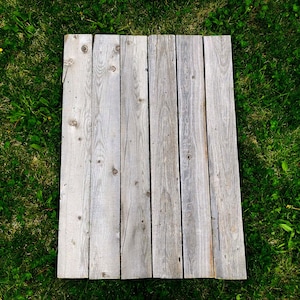 May include: A weathered wooden plank surface with a light gray color. The planks are arranged horizontally and have a rustic appearance.