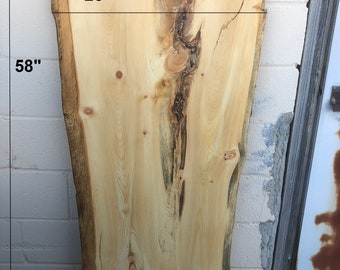 May include: A large, natural wood slab with a live edge. The slab is 58 inches long, 26 inches wide, and 1 1/2 inches thick. The wood has a light brown color with dark brown knots and grain patterns. The slab is labeled "LP1".