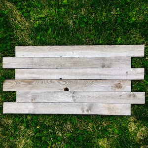 May include: A weathered wooden sign made of six horizontal planks, laid out on a bed of green grass.